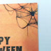 Ευχετήρια κάρτα πορτοκαλί Halloween με ιστούς αράχνης και μαύρο κείμενο “Happy Halloween”