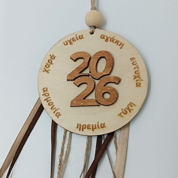 Λεπτομέρεια ξύλινης πινακίδας γουριού 2026 με χαραγμένες ευχές